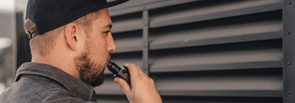Un débutant avec une cigarette électronique tient un téléphone portable, cherchant des conseils d'utilisation.