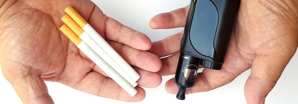 Deux mains tenant une cigarette et une cigarette électronique, soulignant le contraste entre les cigarettes traditionnelles et l'option plus sûre du vapotage.